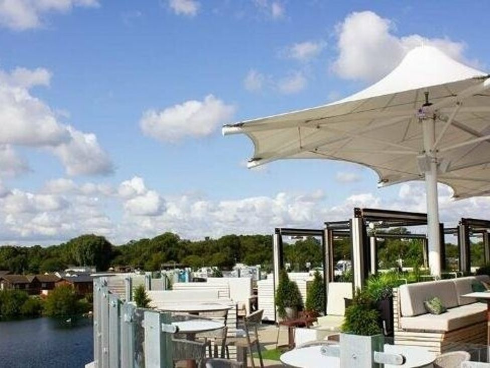 an outdoor seating area with umbrellas overlooking a body of water at Tattershall Lakes Country Park - Holiday Accommodation 16605, Tattershall