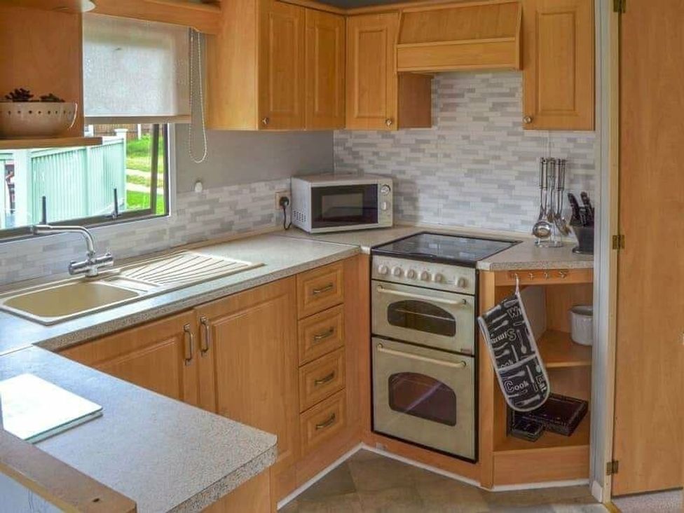 a kitchen with wooden cabinets and a stove at Beach Haven Caravan Park - Holiday Accommodation 16700 in Bacton