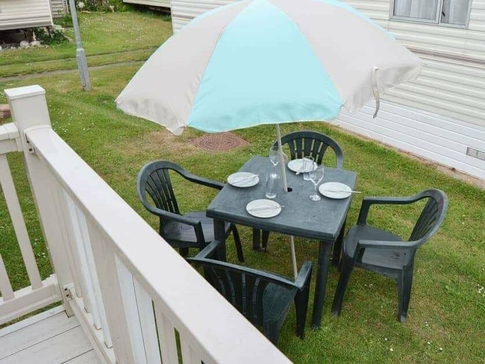 a table with chairs and an umbrella on grass at Beach Haven Caravan Park - Holiday Accommodation 16700, Bacton