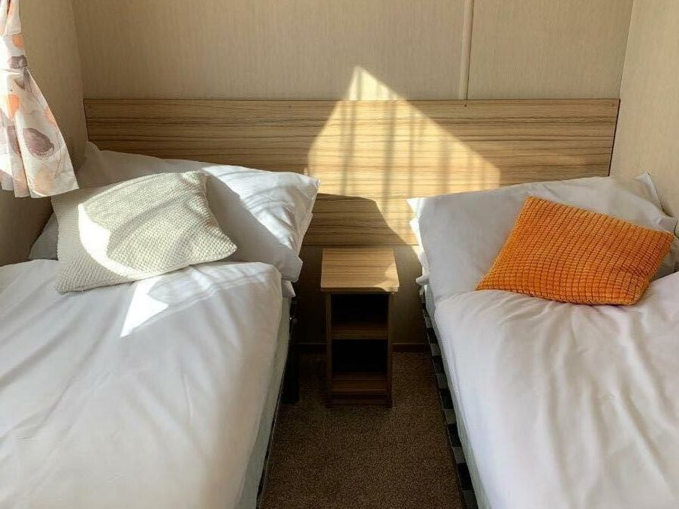 a bedroom with two single beds and a small wooden nightstand at Alberta Holiday Park - Holiday Accommodation 16770 in Whitstable
