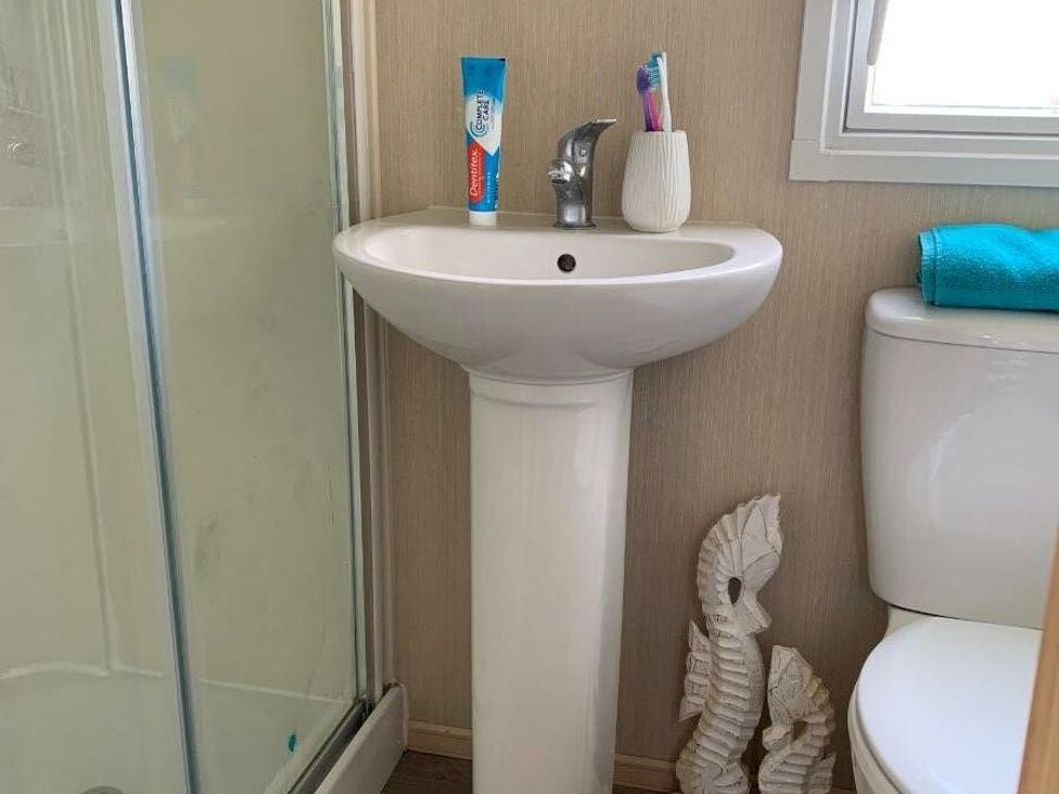 a bathroom with a white pedestal sink and toiletries at Alberta Holiday Park - Holiday Accommodation 16770 in Whitstable