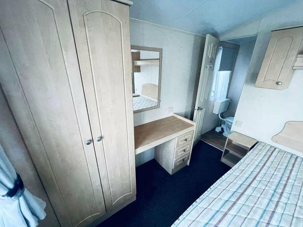 a bedroom with a wardrobe, desk, mirror, and bed at WigBay Holiday Park - Holiday Accommodation 16774 Stranraer