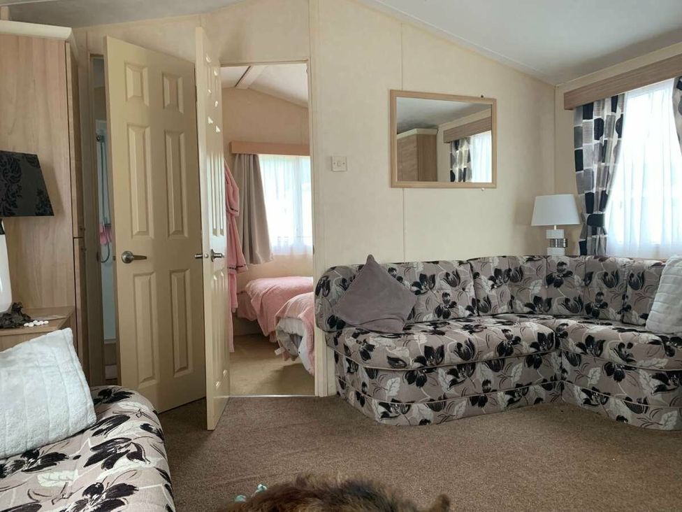 a living room with floral patterned sofas and an open door leading to a pink bedroom at WigBay Holiday Park - Holiday Accommodation 16774, Stranraer