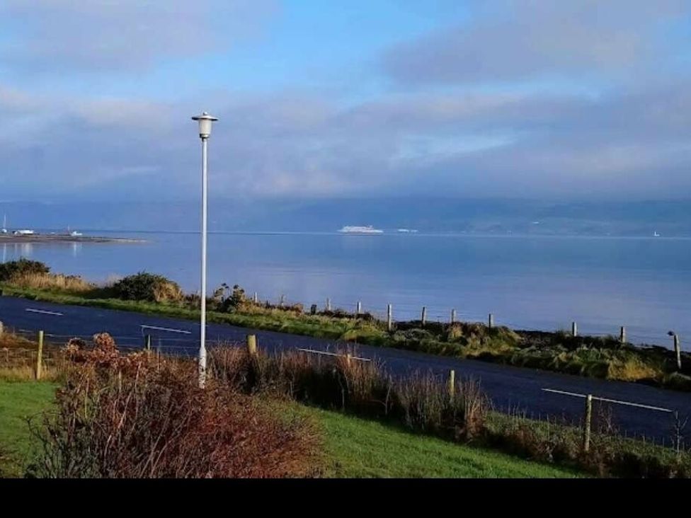 a view of water with a distant ship and a road beside it at WigBay Holiday Park - Holiday Accommodation 16774, Stranraer