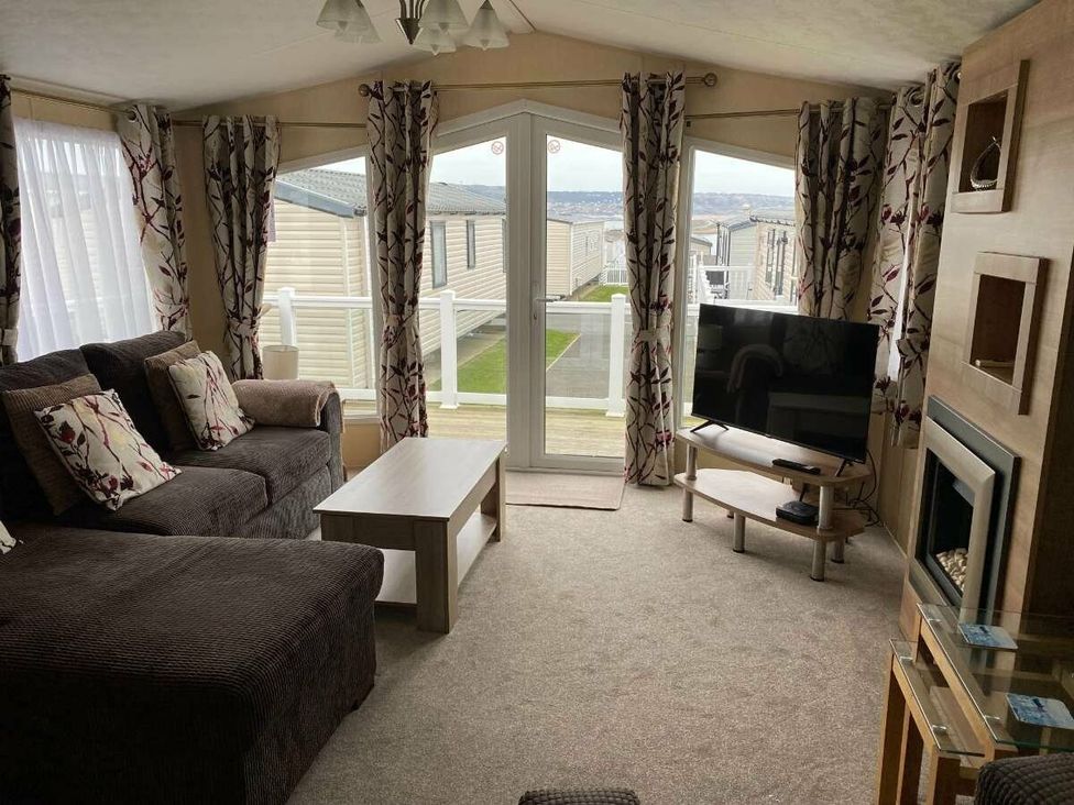 a living room with a sofa, coffee table, television, and large windows at Chesil Beach Holiday Park - Holiday Accommodation 16933 Weymouth