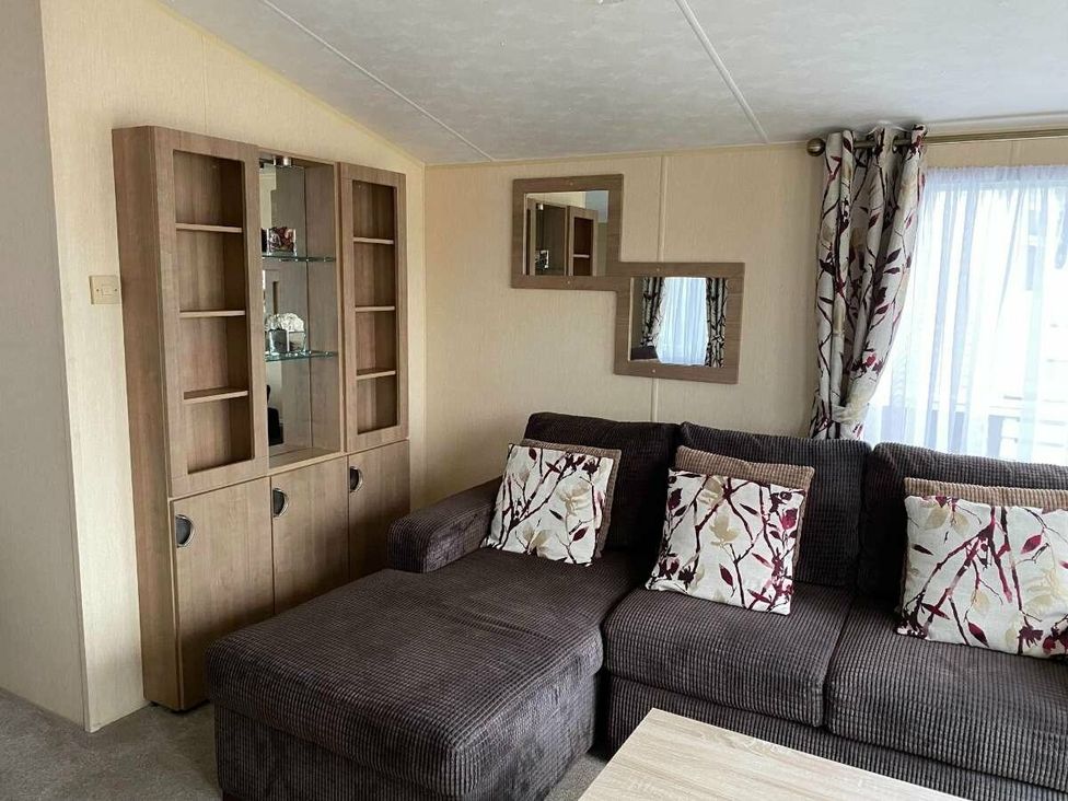 a living room with a brown sectional sofa and a display cabinet at Chesil Beach Holiday Park - Holiday Accommodation 16933 in Weymouth