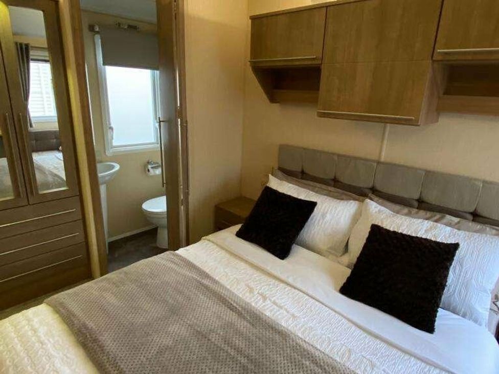 a bedroom with a bed, decorative pillows, and an adjoining bathroom at Chesil Beach Holiday Park - Holiday Accommodation 16933 in Weymouth