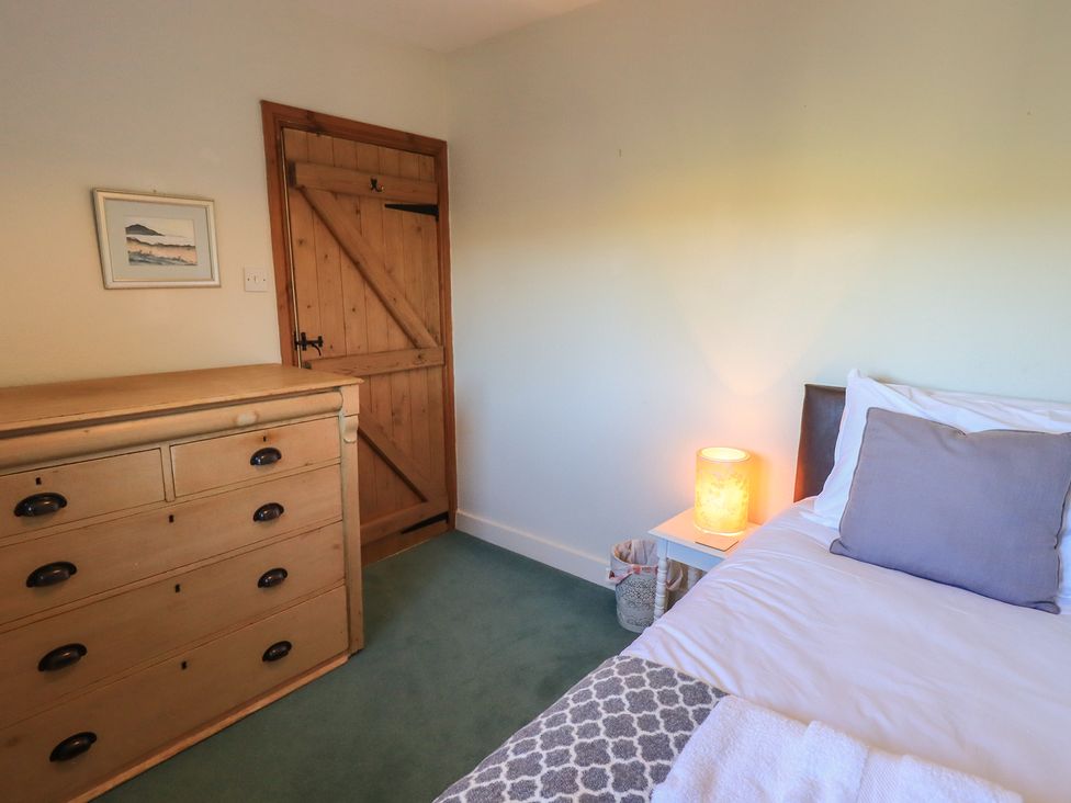 A bedroom with a bed, chest of drawers, and a lamp at 2 Lupton Hall Cottages in Carnforth