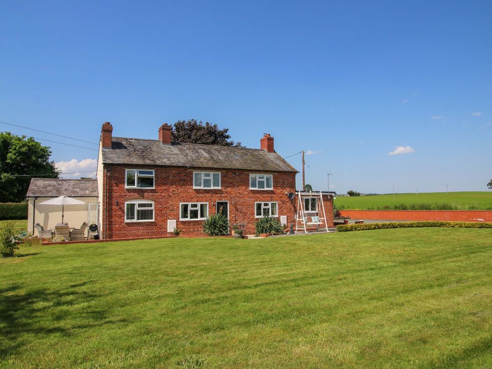 A brick house with a lawn and patio furniture at Fron-Haul near Llansantffraidd-Ym-Mechain