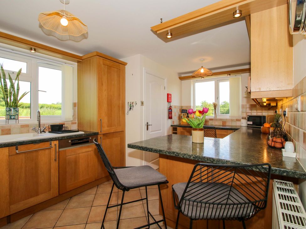 A kitchen with wooden cabinets and bar stools at Fron-Haul Near Llansantffraidd-Ym-Mechain