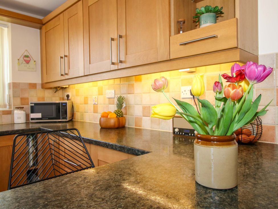 A kitchen with a microwave and flowers on the counter at Fron-Haul near Llansantffraidd-Ym-Mechain