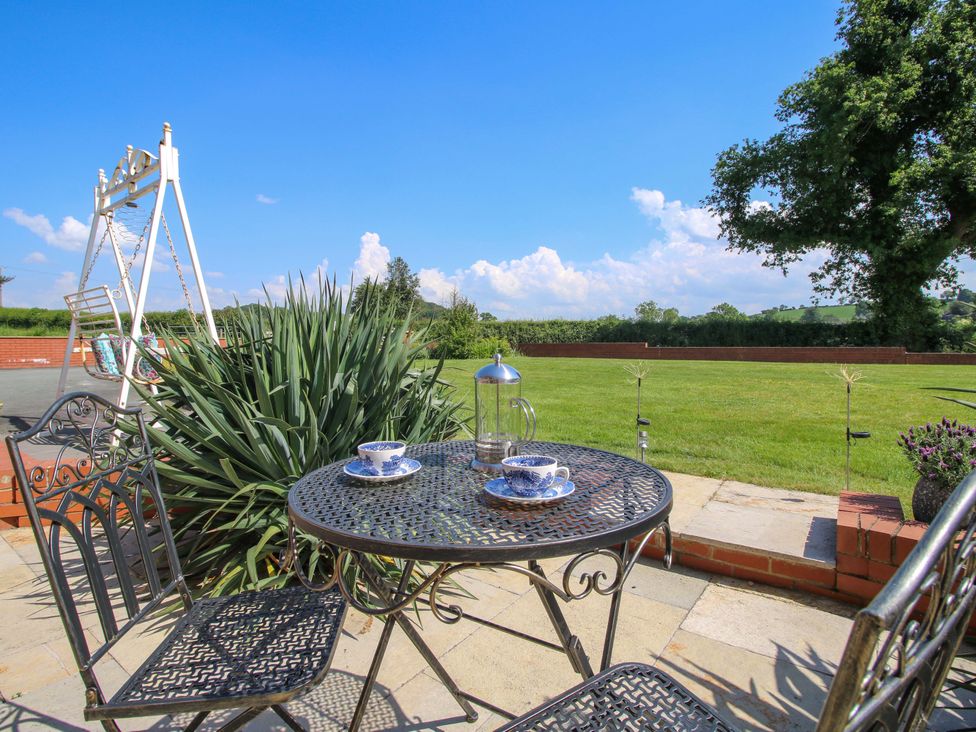 A garden with a table and chairs and a swing set at Fron-Haul near Llansantffraidd-Ym-Mechain