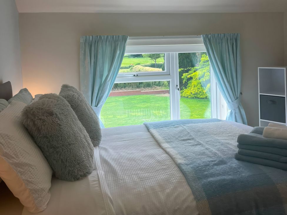 A bedroom with a bed and a window overlooking the garden at Fron-Haul near Llansantffraid-Ym-Mechain