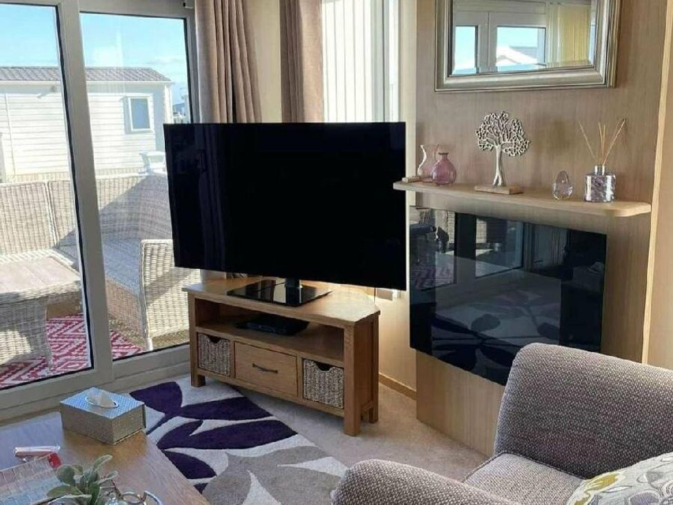 a living room with a television on a stand and a window at Golden Anchor Holiday Park - Holiday Accommodation 17383 in Skegness