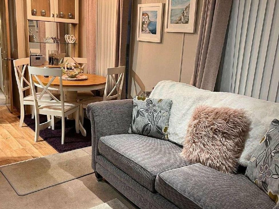 a living room with a gray sofa and a dining area with a round table at Golden Anchor Holiday Park - Holiday Accommodation 17383, Skegness