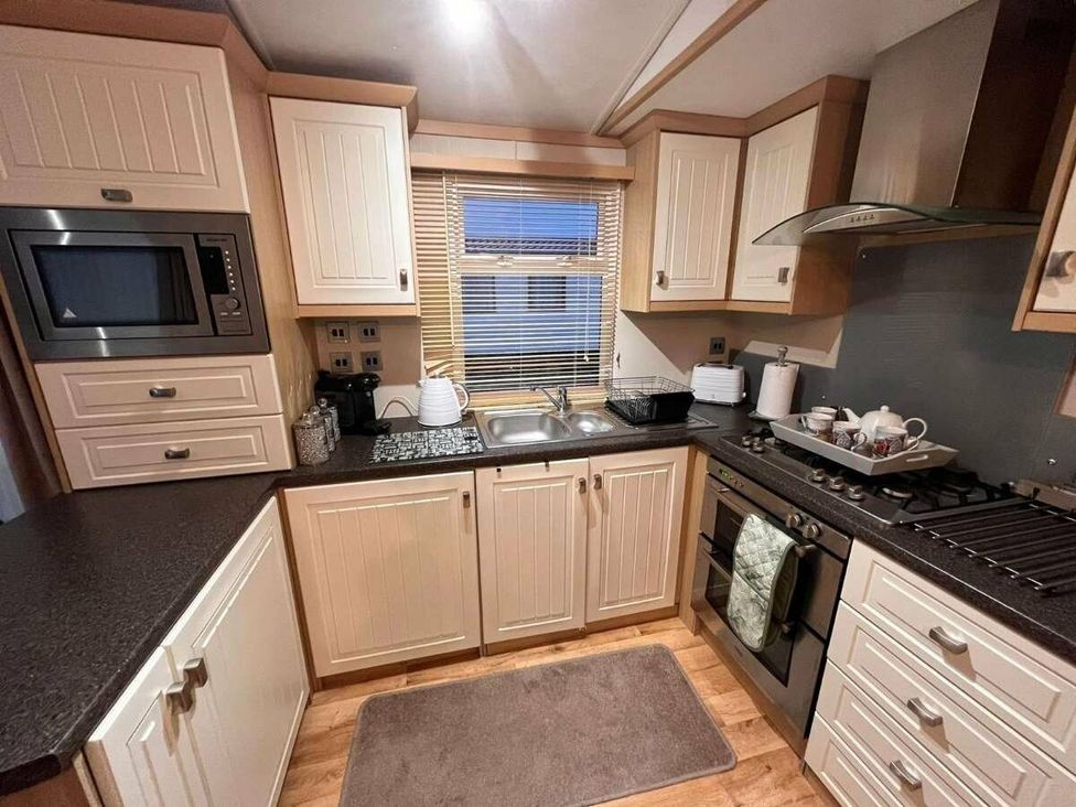 a kitchen with wooden cabinets, sink, stove, and microwave at Golden Anchor Holiday Park - Holiday Accommodation 17383, Skegness