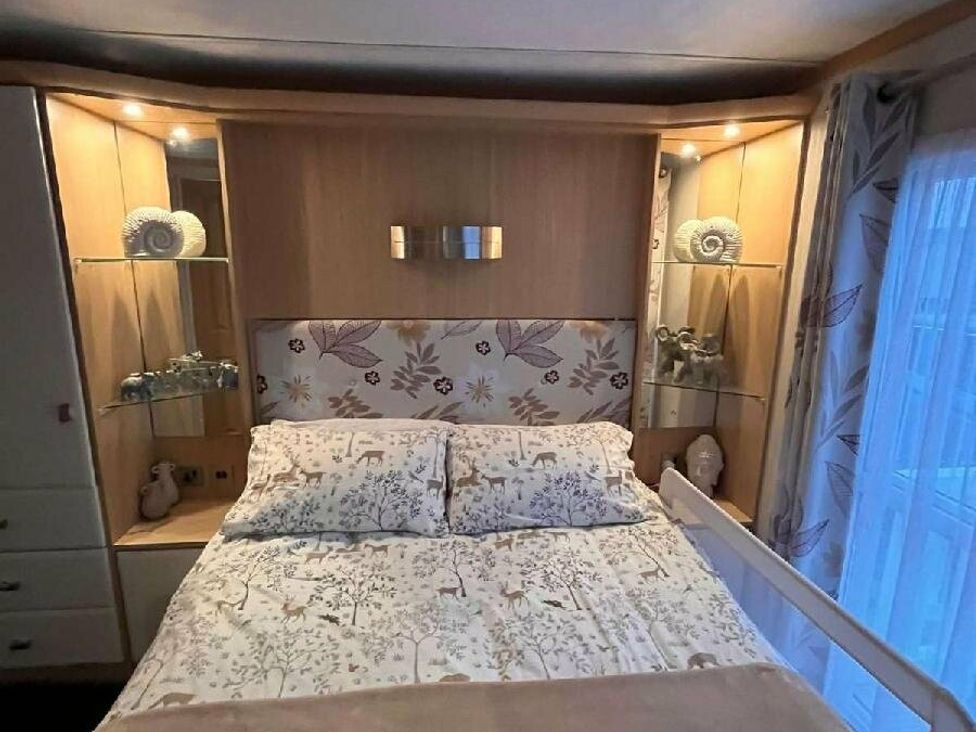a bedroom with a bed adorned with floral bedding and built-in shelves displaying decorative items at Golden Anchor Holiday Park - Holiday Accommodation 17383 in Skegness