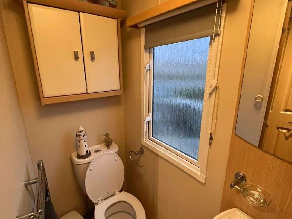 a small bathroom with a toilet, a window, shelves, and a towel rack at Golden Anchor Holiday Park - Holiday Accommodation 17383, Skegness