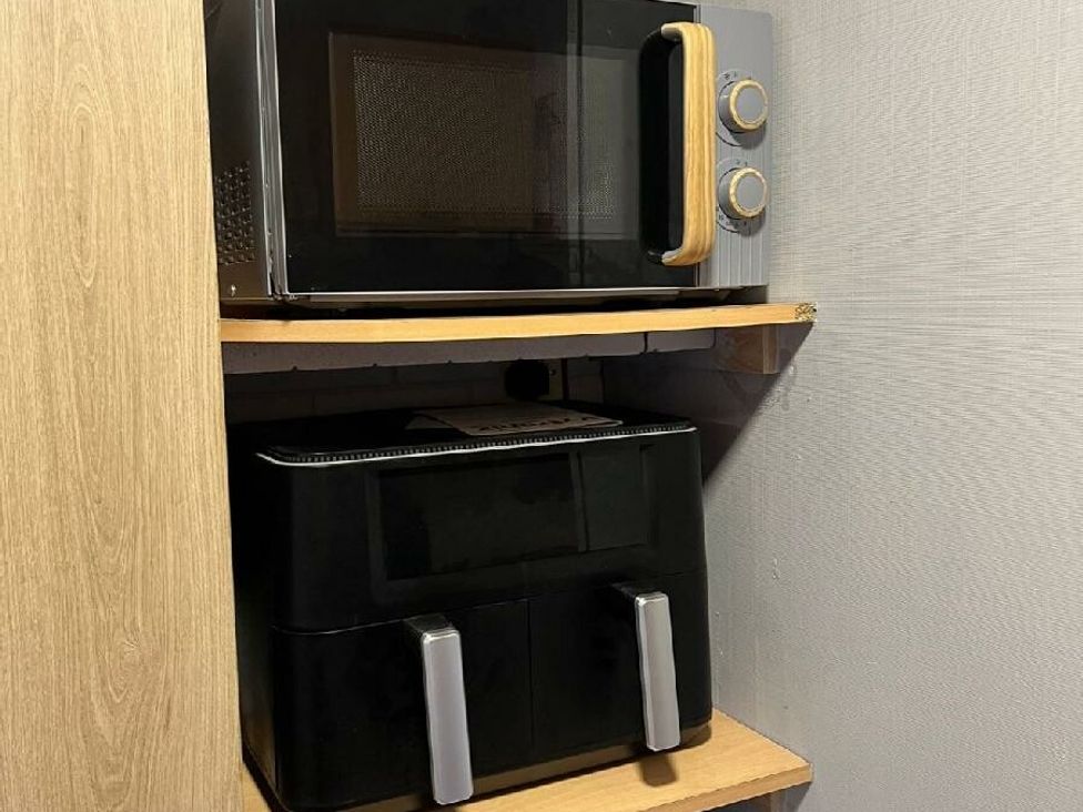 a microwave on a shelf above a black appliance with two handles at Three Lochs Holiday Park - Holiday Accommodation 17424, Stranraer