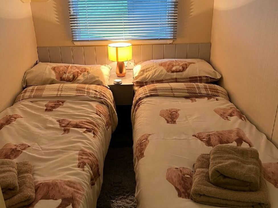 a bedroom with two single beds, light brown bedding featuring animal patterns, and a lamp at Three Lochs Holiday Park - Holiday Accommodation 17424 in Stranraer