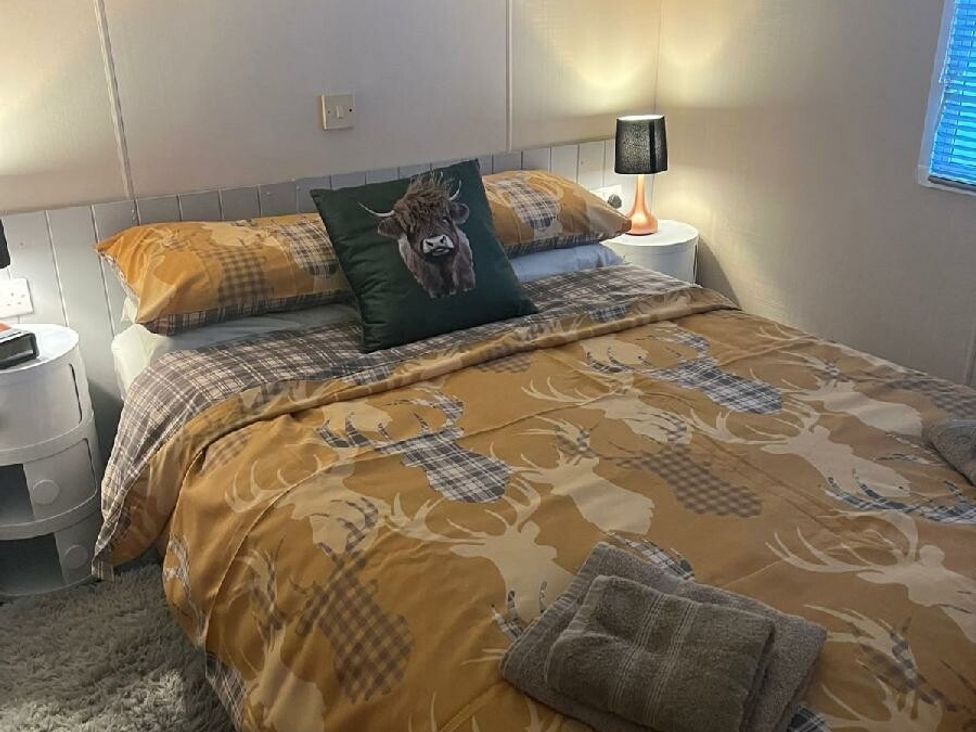 a bedroom with a bed featuring patterned bedding and a decorative pillow at Three Lochs Holiday Park - Holiday Accommodation 17424, Stranraer
