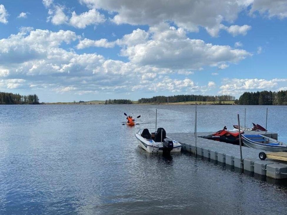 a calm lake with boats at a dock and kayakers at Three Lochs Holiday Park - Holiday Accommodation 17424, Stranraer