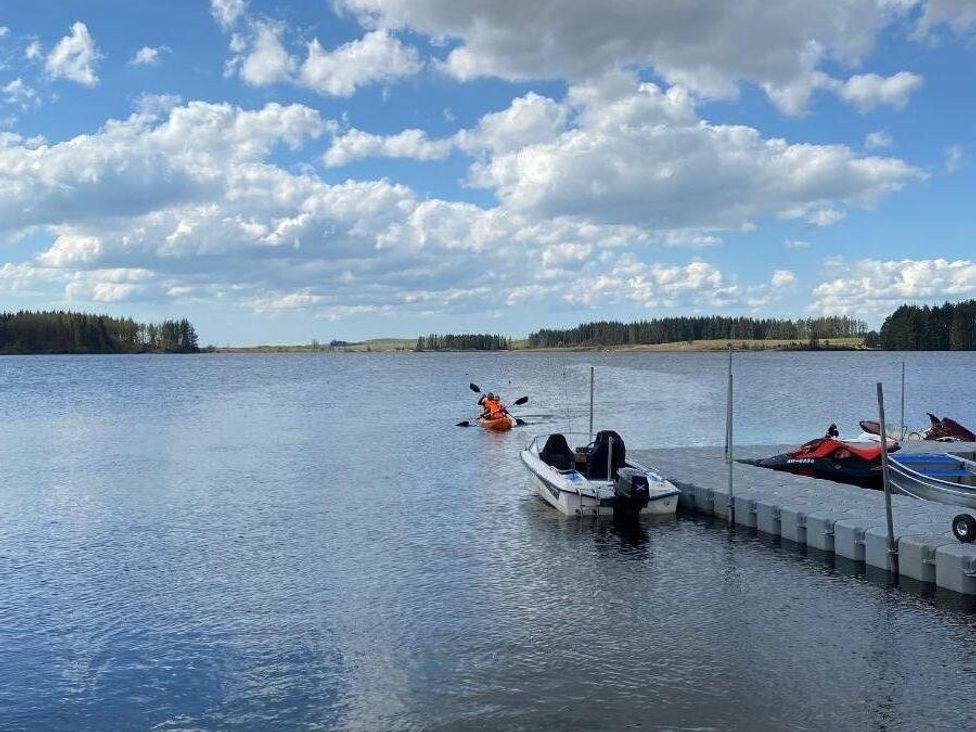 a lake with a kayaker and boats on a dock at Three Lochs Holiday Park - Holiday Accommodation 17424 in Stranraer