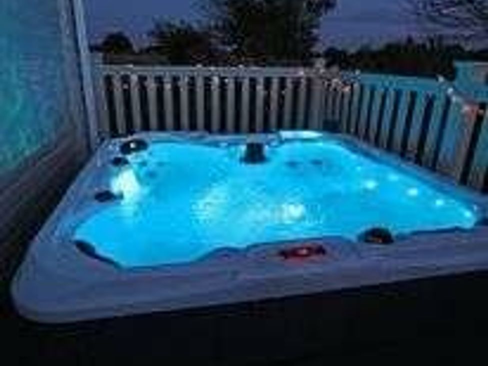 a hot tub illuminated with blue lights on a deck with a railing at Tattershall Lakes Country Park - Holiday Accommodation 17807 in Tattershall