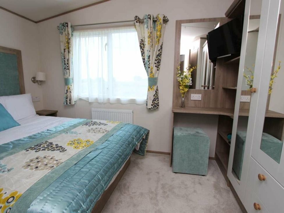 a bedroom with a bed, a mirror, and a small chair at Tattershall Lakes Country Park - Holiday Accommodation 17807, Tattershall