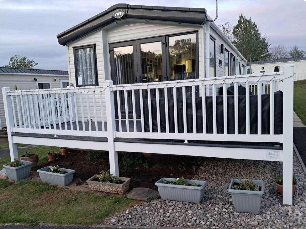 a holiday home with a white deck and planters at Golden Sands Holiday Park - Holiday Accommodation 18951 in Dawlish