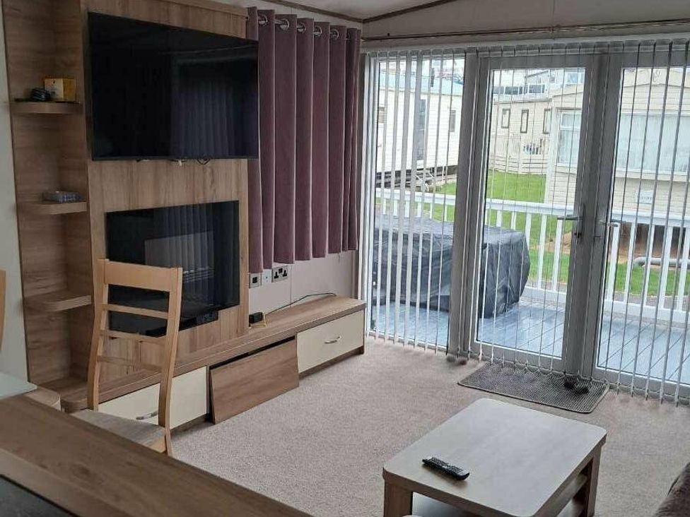 a living room with a TV, sliding glass doors, and a table at Golden Sands Holiday Park - Holiday Accommodation 18951, Dawlish