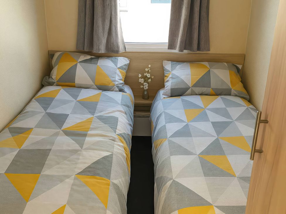 A bedroom with two beds and a small table with flowers at Golden Gate Holiday Centre - Holiday Accommodation 19059 Towyn