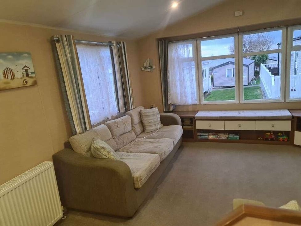 a living room with a sofa, curtains, and windows overlooking a garden at Littlesea Holiday Park - Holiday Accommodation 19270 in Weymouth