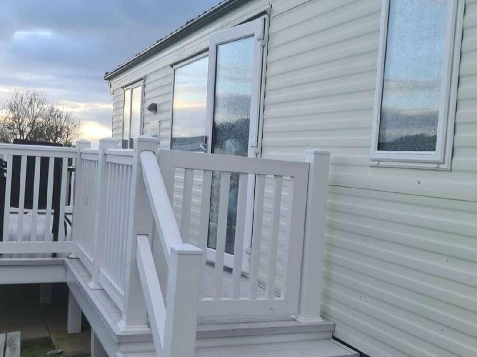 a white exterior of a mobile home with a wooden deck and railing at Littlesea Holiday Park - Holiday Accommodation 19270 in Weymouth