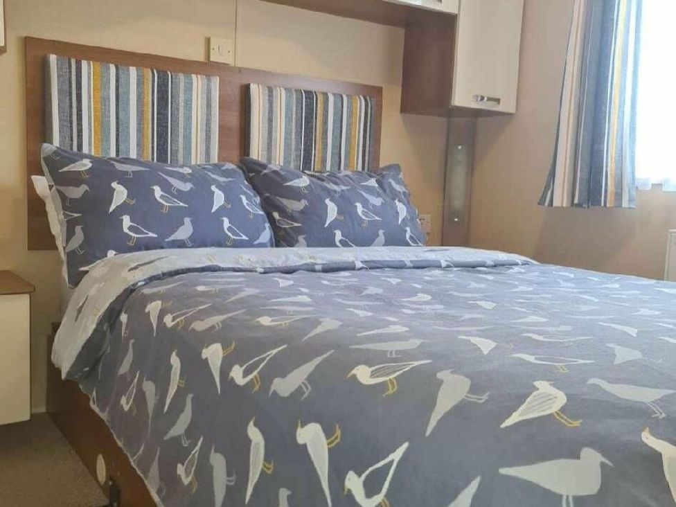 a bedroom with a bed featuring bird-patterned bedding and striped headboard at Littlesea Holiday Park - Holiday Accommodation 19270, Weymouth