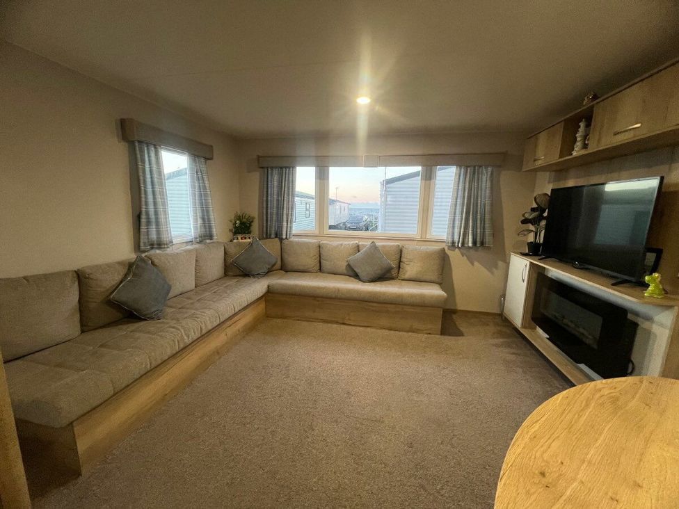 a living room with a sectional sofa, windows, and a TV unit at Golden Sands Kinmel Bay - Holiday Accommodation 20528 in Rhyl