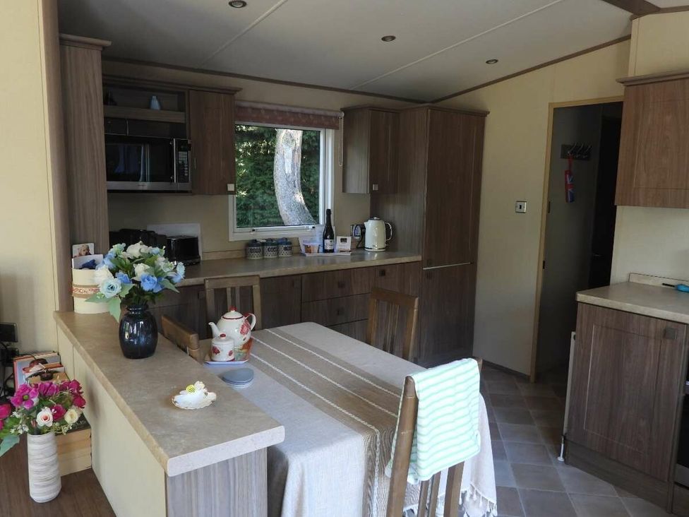 a kitchen with cabinets, a dining table, and appliances at Kelling Heath Holiday Park - Holiday Accommodation 20665 in Weybourne