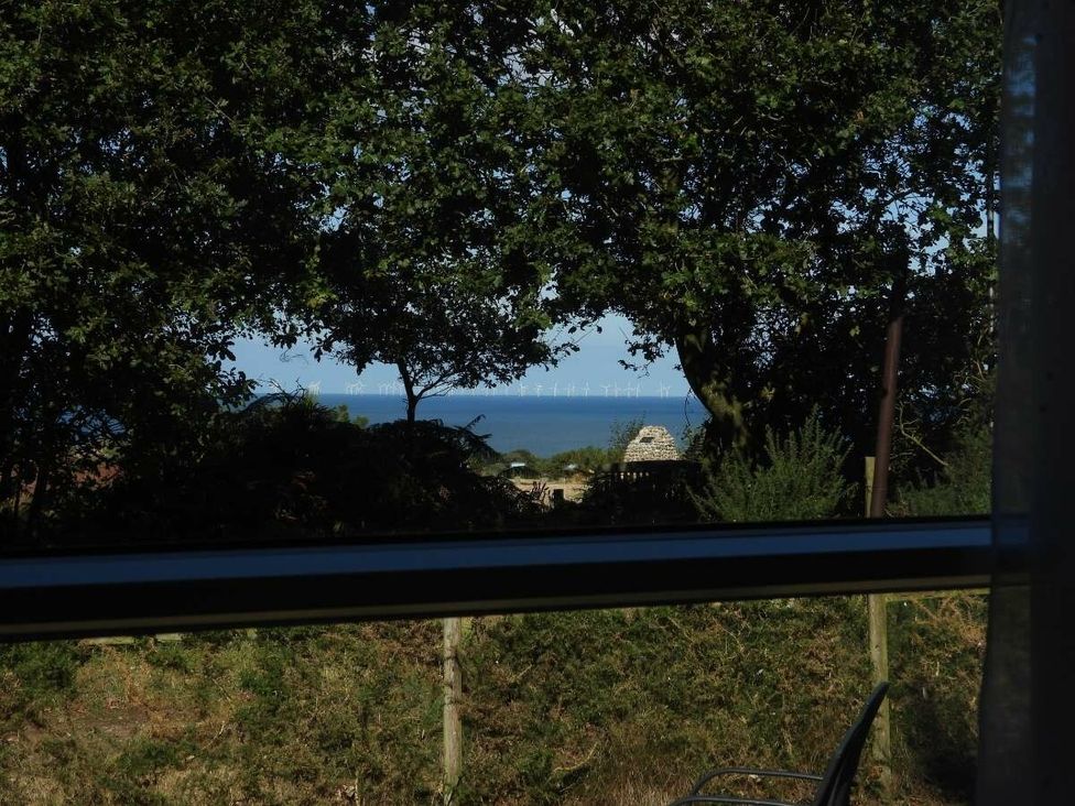 a view of the ocean with wind turbines visible through trees at Kelling Heath Holiday Park - Holiday Accommodation 20665 in Weybourne