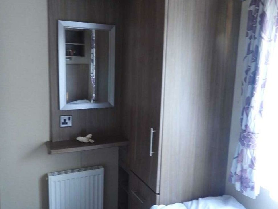 a corner of a room with a wooden wardrobe and mirror at Kelling Heath Holiday Park - Holiday Accommodation 20665, Weybourne