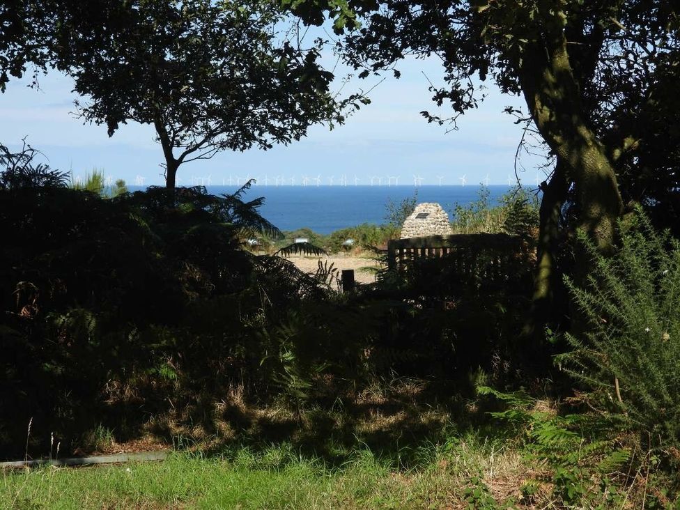 a view of wind turbines in the distance over the ocean framed by trees and vegetation at Kelling Heath Holiday Park - Holiday Accommodation 20665 in Weybourne