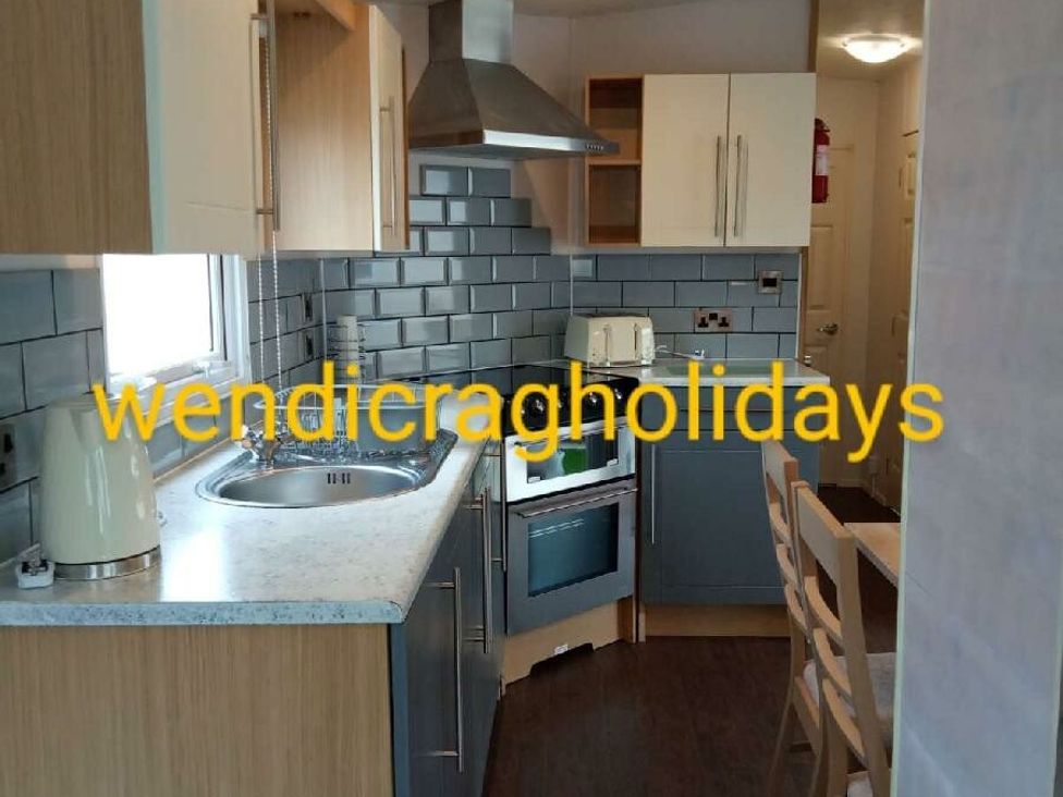 a kitchen with cabinets, a sink, an oven, and a dining table at Ty Mawr Holiday Park - Holiday Accommodation 20936, Towyn