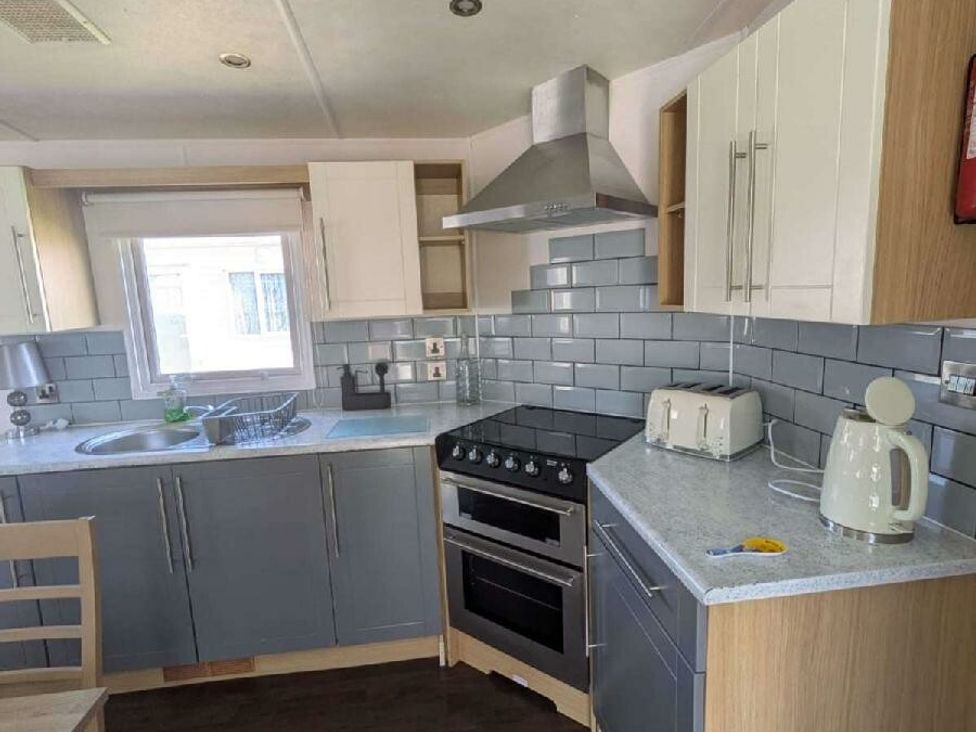 a kitchen with grey and white cabinets, silver appliances, and a window at Ty Mawr Holiday Park - Holiday Accommodation 20936, Towyn