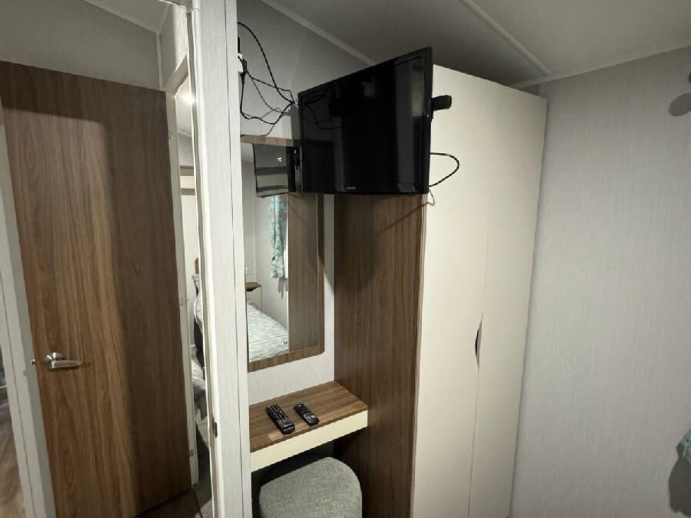 a room with a mounted TV, a small table, and a mirror at Butlins Skegness - Holiday Accommodation 21028 in Skegness