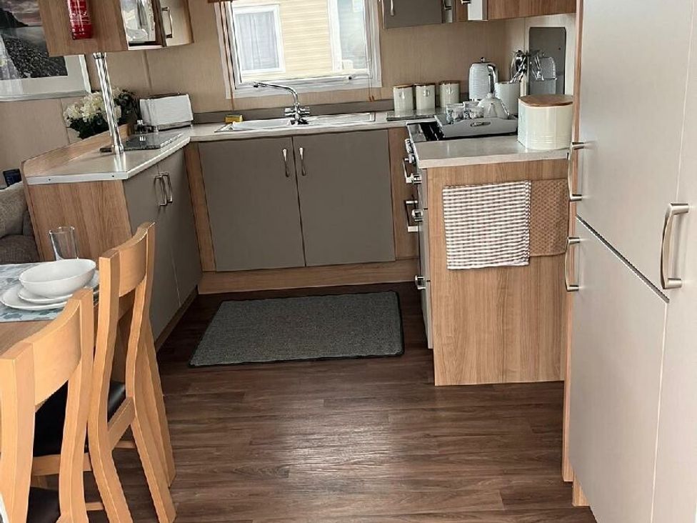 a kitchen with wooden cabinets and a dining table at Eastgate Caravan Park - Holiday Accommodation 21087 in Ingoldmells