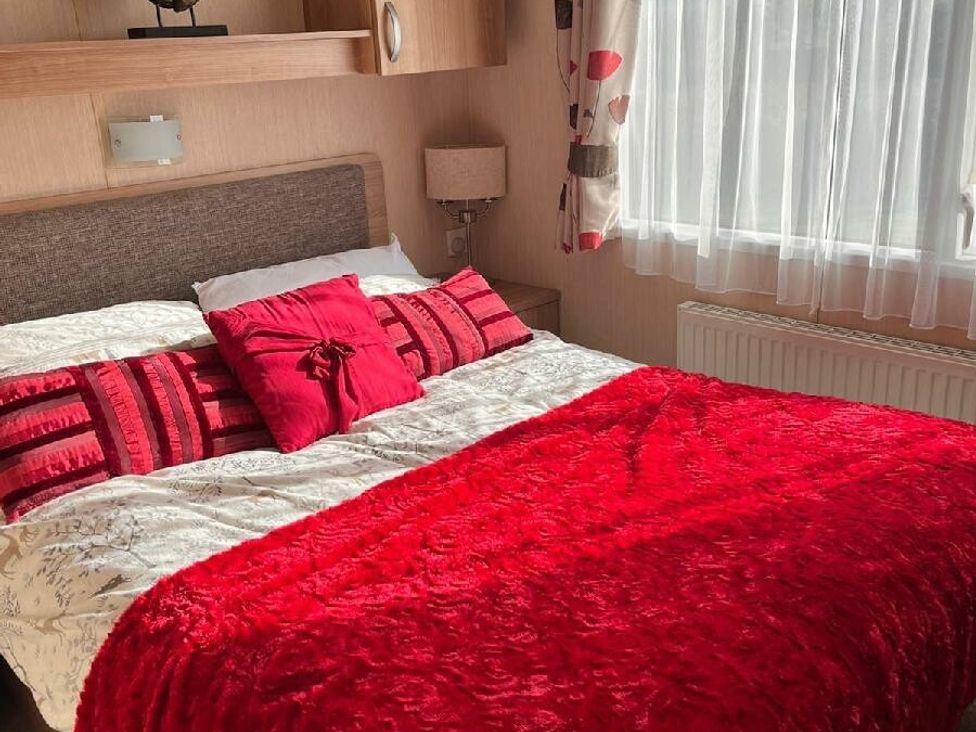 a bedroom featuring a bed with red bedding and cushions at Eastgate Caravan Park - Holiday Accommodation 21087 in Ingoldmells