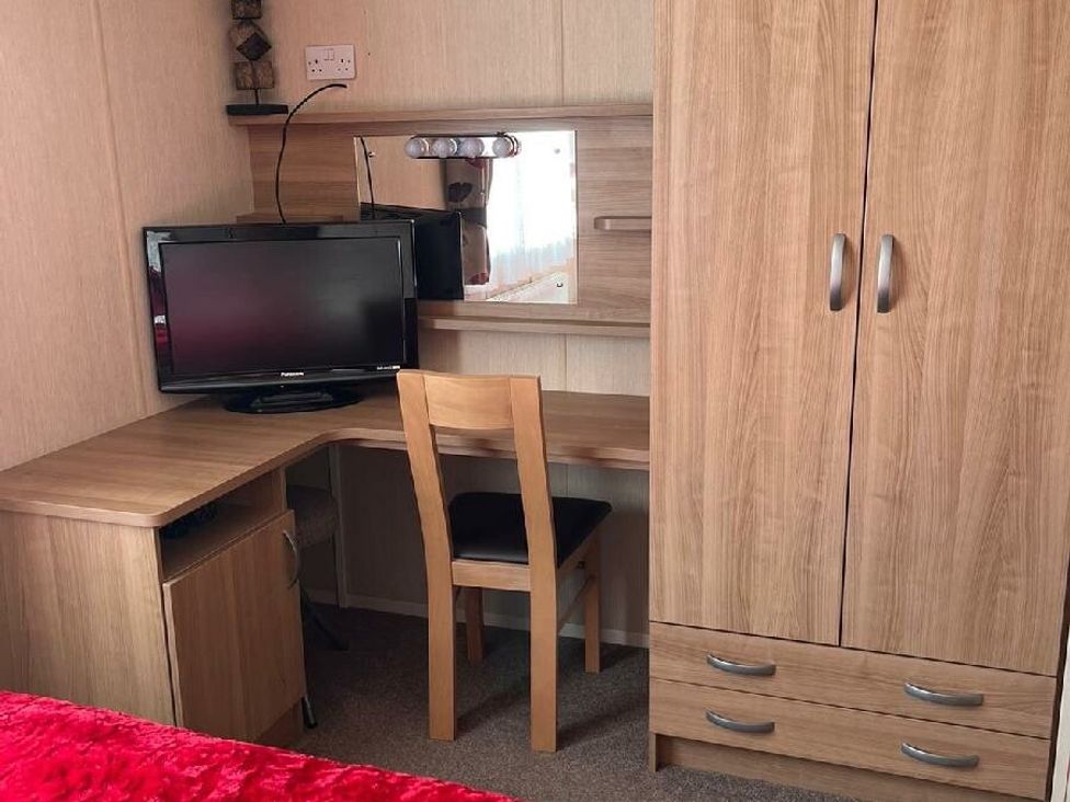 a wooden desk with a chair and a television underneath a mirror at Eastgate Caravan Park - Holiday Accommodation 21087 in Ingoldmells