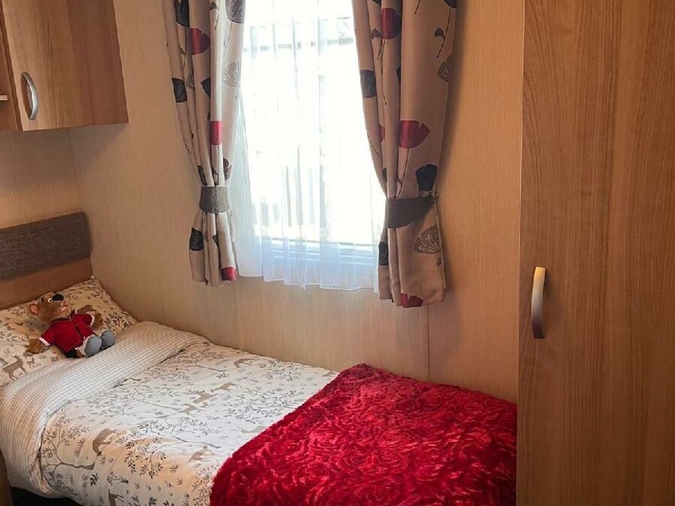 a small bedroom with a single bed, curtains, and a wardrobe at Eastgate Caravan Park - Holiday Accommodation 21087 in Ingoldmells