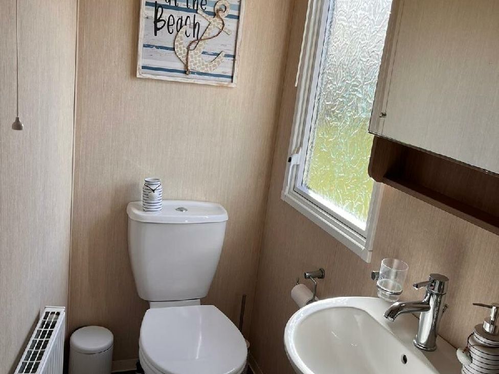 a bathroom with a toilet, sink, and a decorative beach-themed sign at Eastgate Caravan Park - Holiday Accommodation 21087 in Ingoldmells