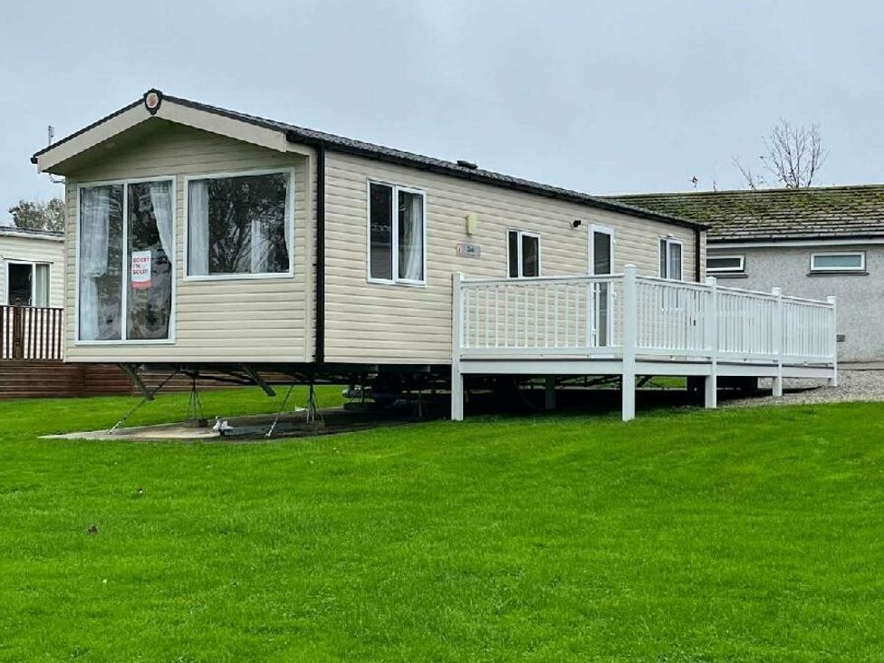 a static caravan with a deck on grass at Trevella Park - Holiday Accommodation 21105 in Crantock