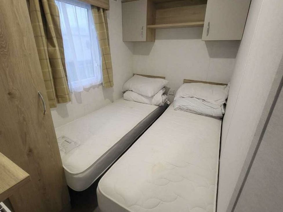 a bedroom with two single beds, a window with curtains, and storage shelves at Ty Mawr Holiday Park - Holiday Accommodation 21121, Ty Mawr